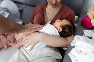 A mão do pai sobre o bebé ao colo da mãe